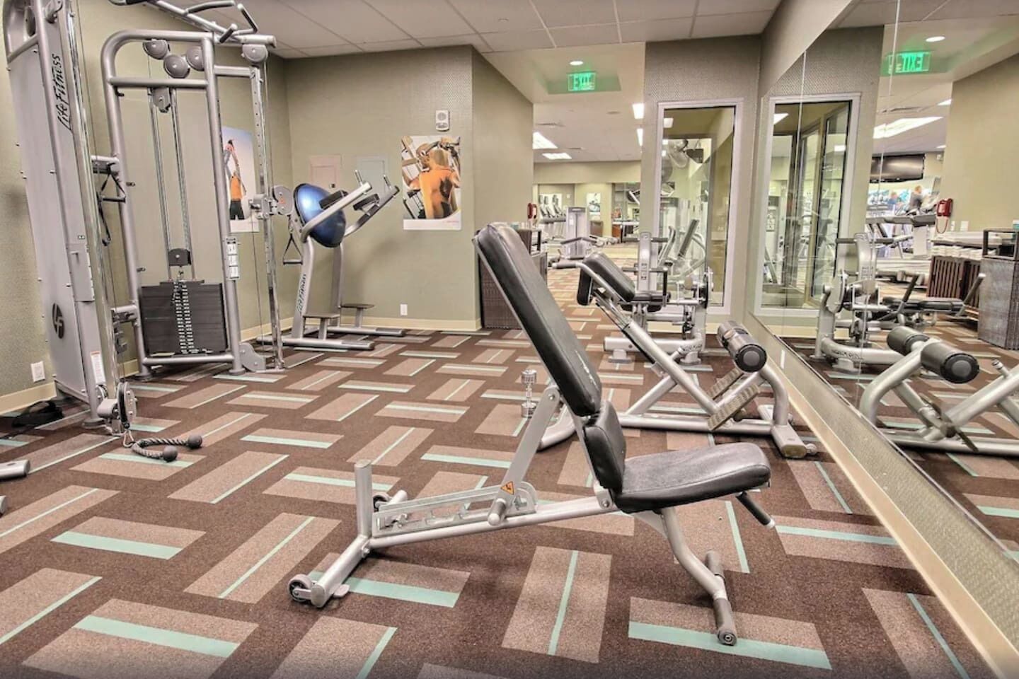 A gym with exercise equipment, mirrors, and patterned carpet.