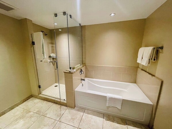 A modern bathroom with a glass-enclosed shower, a white bathtub, and beige tiled walls.