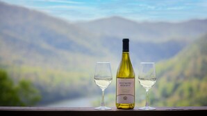 A bottle of Biltmore Reserve Chardonnay and two glasses on a wooden ledge with a blurred mountain view in the background. - Lake Life Mountain & Lake Views, Hot Tub, & Dock (Butler)