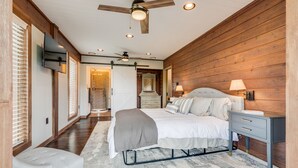 A bedroom with a bed, bedside tables, a nightstand, a ceiling fan, and wooden walls. - Lake Life Mountain & Lake Views, Hot Tub, & Dock (Butler)