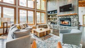 A spacious living room with a stone fireplace, large windows, and a cozy seating area. - Lake Life Mountain & Lake Views, Hot Tub, & Dock (Butler)