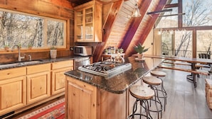 A kitchen with wooden cabinets, a granite countertop, a stove, and a large window overlooking a forest.