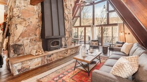 A cozy living room with a stone fireplace, wooden beams, a large window, and a comfortable seating area.