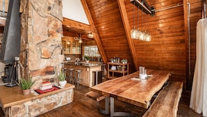 A rustic kitchen with a stone wall, wooden ceiling, and a long wooden table.