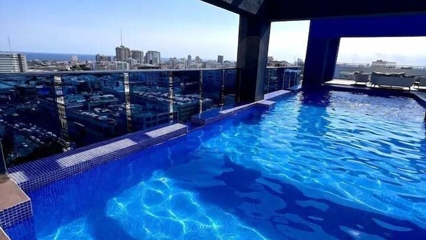 A rooftop infinity pool with a city view, clear blue water, and a modern architectural design.