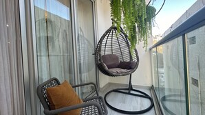 A balcony with a hanging chair, a cushioned chair, and a potted plant.
