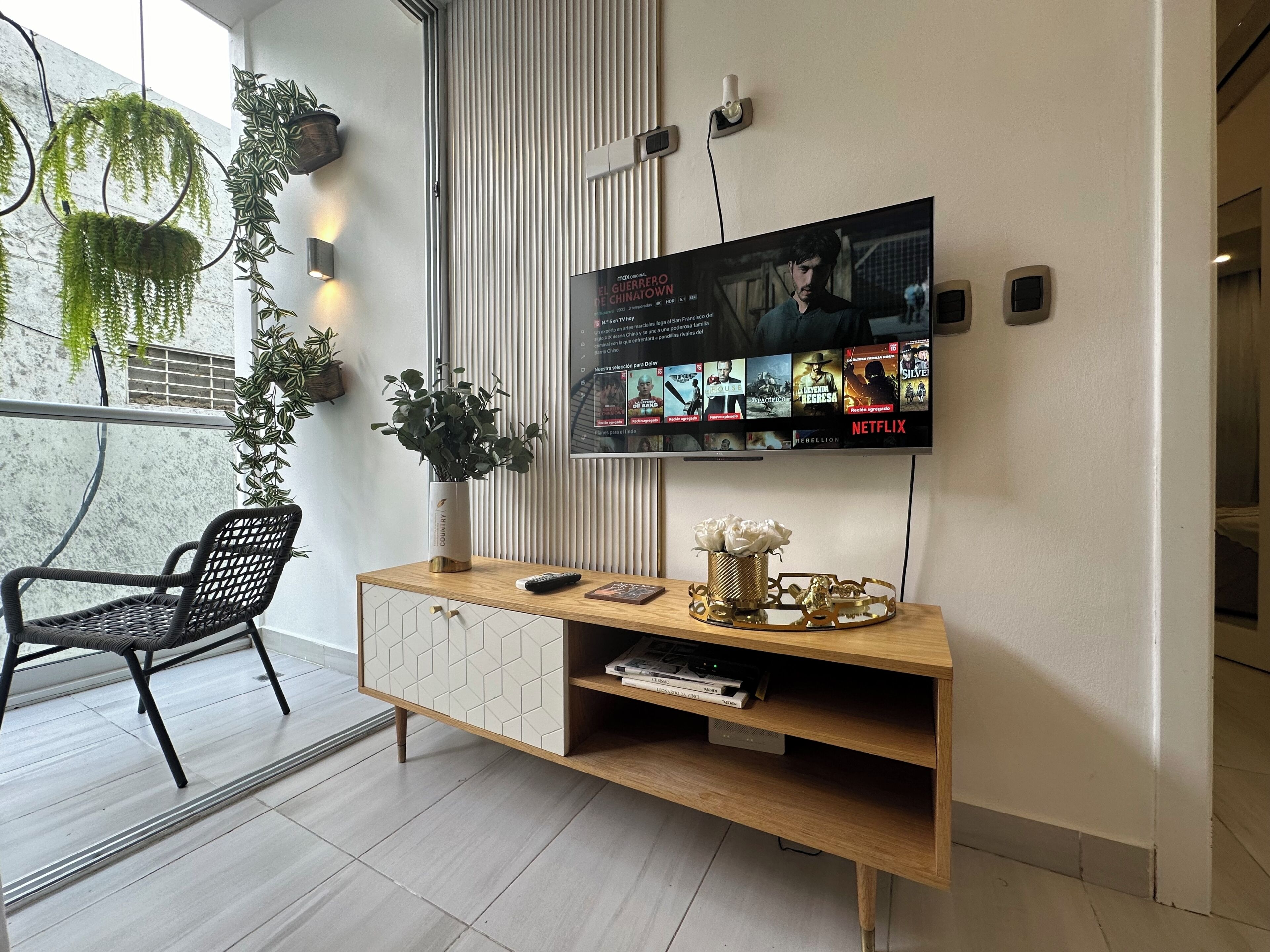 A modern living room with a TV displaying a movie, a black chair, a wooden console, and a potted plant.