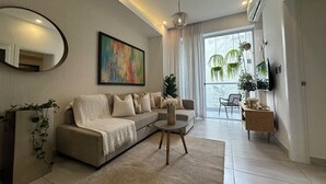 A modern living room with a sofa, a coffee table, a TV, and a large window with curtains.