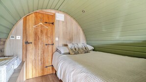 Een kamer met een houten deur, een bed met een witte dekbedovertrek en een kapstok.