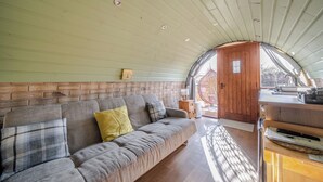 Een gezellig interieur met een houten bankje, een sofa met kussens, een kleine tafel en een deur naar buiten.