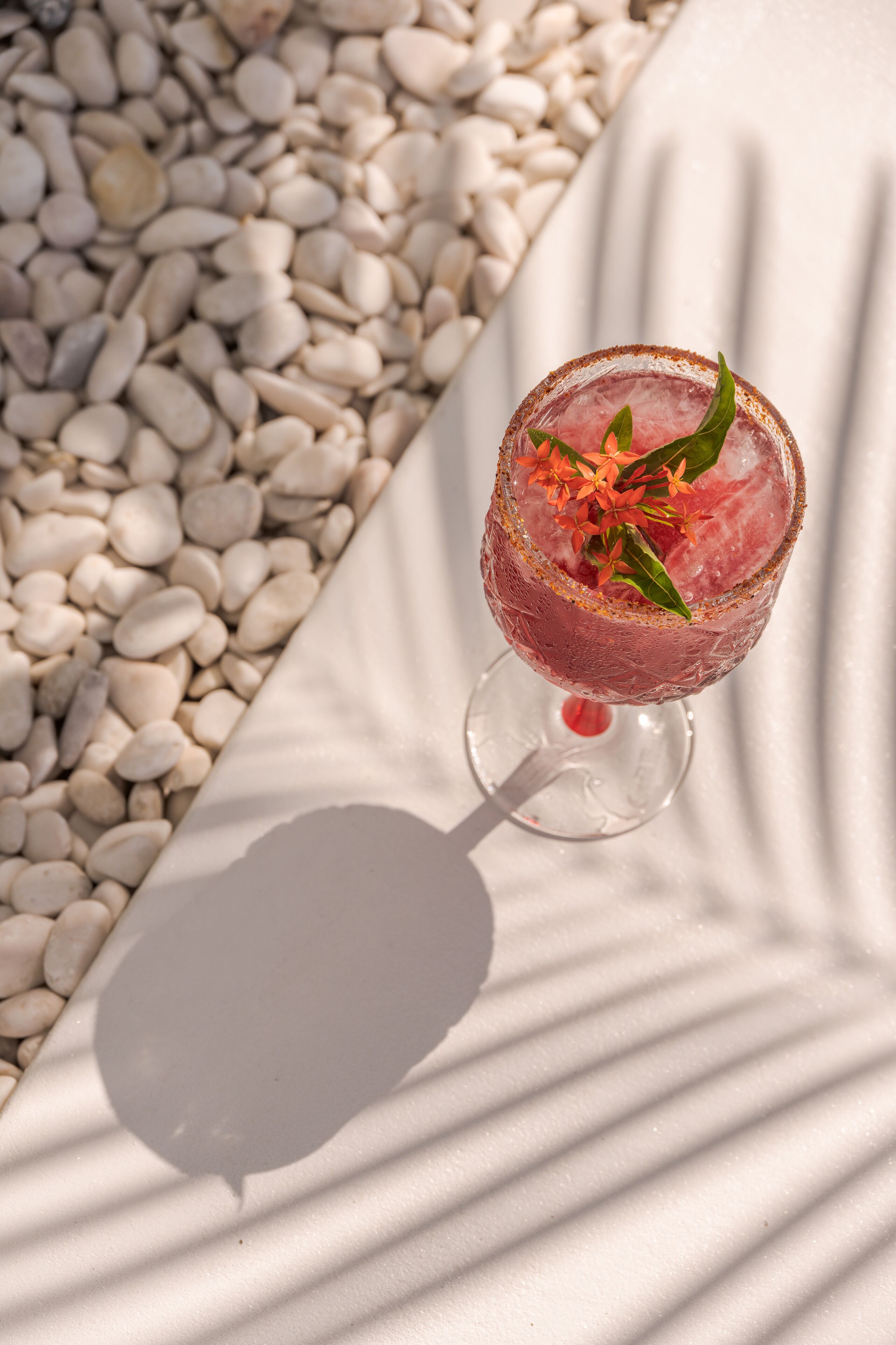 Een cocktailglas met een bloemversiering op een witte ondergrond met kiezels.