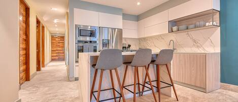 Una cocina moderna con una isla central, taburetes de bar y electrodomésticos integrados.