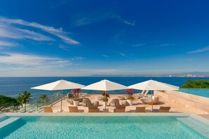 Área da piscina com espreguiçadeiras, guarda-sóis e vista para o oceano.