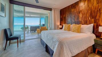 A bedroom with a large bed, a chair, a nightstand, and a view of the ocean through a sliding door.