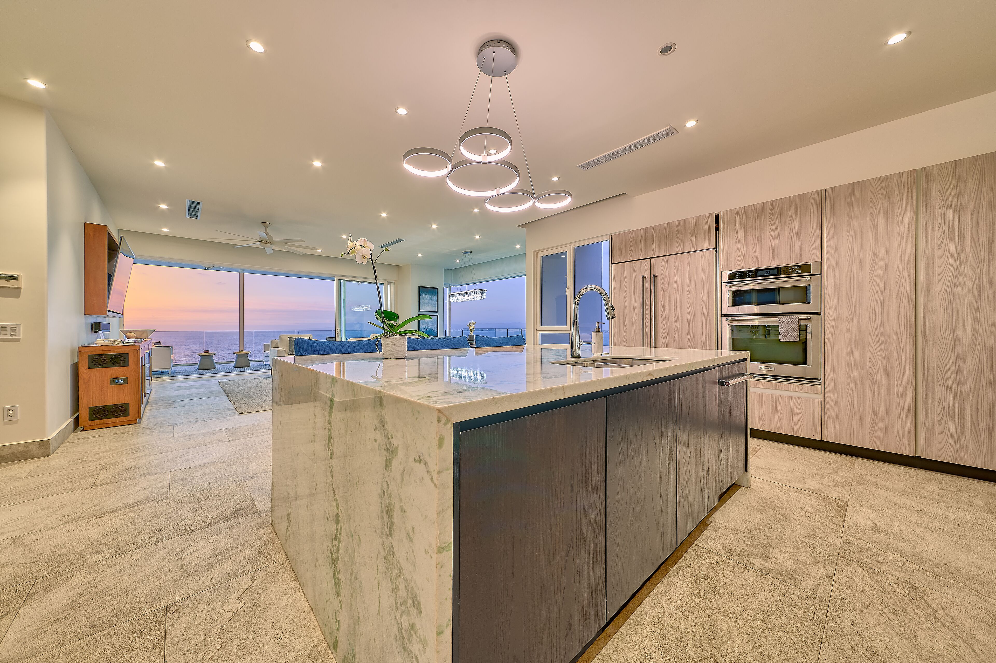 A modern kitchen with a large island, built-in oven, and a view to the outdoors.