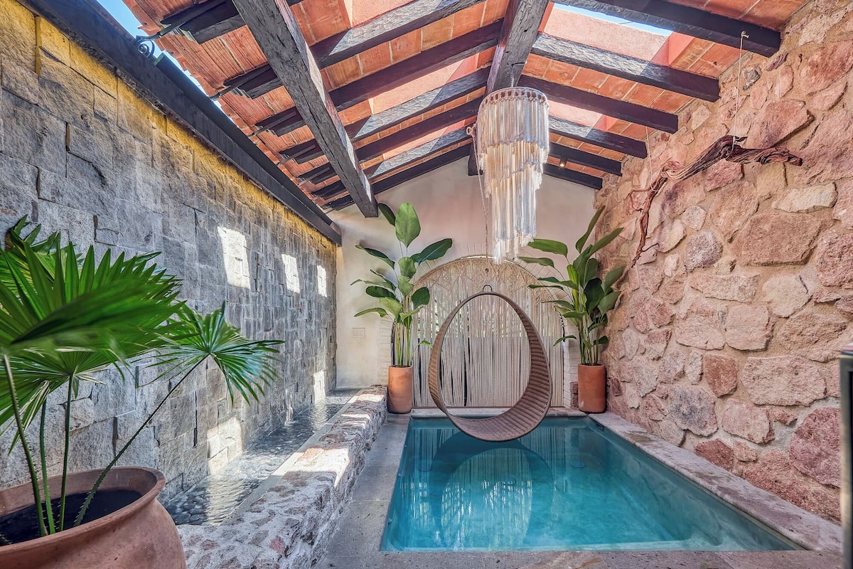 A pool area with a hanging chair, potted plants, and stone walls.