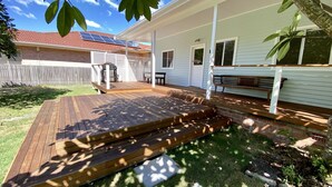 Ein Garten mit einer Holzterrasse, einer überdachten Veranda und einer Ziegelmauer.