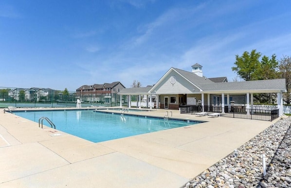A swimming pool with a covered seating area and a building with a white roof in the background.