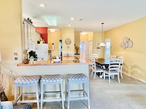 A modern kitchen with white cabinets, a wooden island, and a dining area with white chairs.