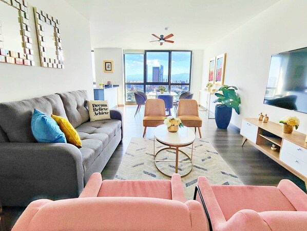 A modern living room with a grey sofa, a pink armchair, a round coffee table, and a TV on the right.