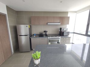 A modern kitchen with a stainless steel refrigerator, a microwave, and a stove. There is a potted plant on the counter.
