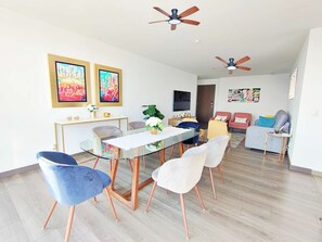 Een moderne woonkamer met een glazen eettafel, twee plafondventilatoren en een zithoek.