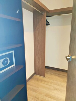 Een kamer met een houten vloer, een blauwe muur met een beveiligingspaneel, en een deur met een handgreep.