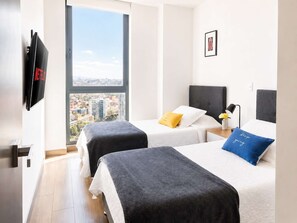 Een hotelkamer met twee bedden, een televisie, uitzicht over de stad en een ingelijst beeld aan de muur.