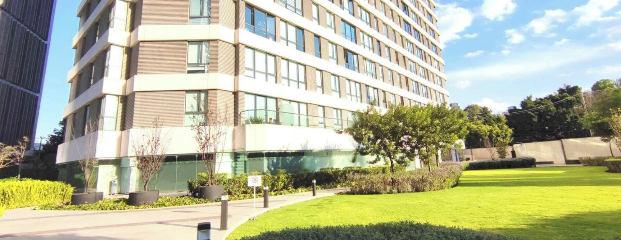 A modern multi-story building with a glass facade, surrounded by a well-maintained lawn and a few trees.