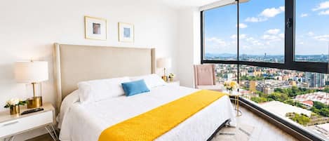 A hotel room with a large bed, two bedside lamps, a nightstand, a window with a city view, and a ceiling fan.