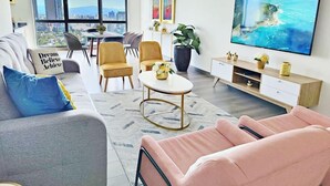 Un salon moderne avec un canapé, des fauteuils, une table basse, un téléviseur et une vue sur la ville.