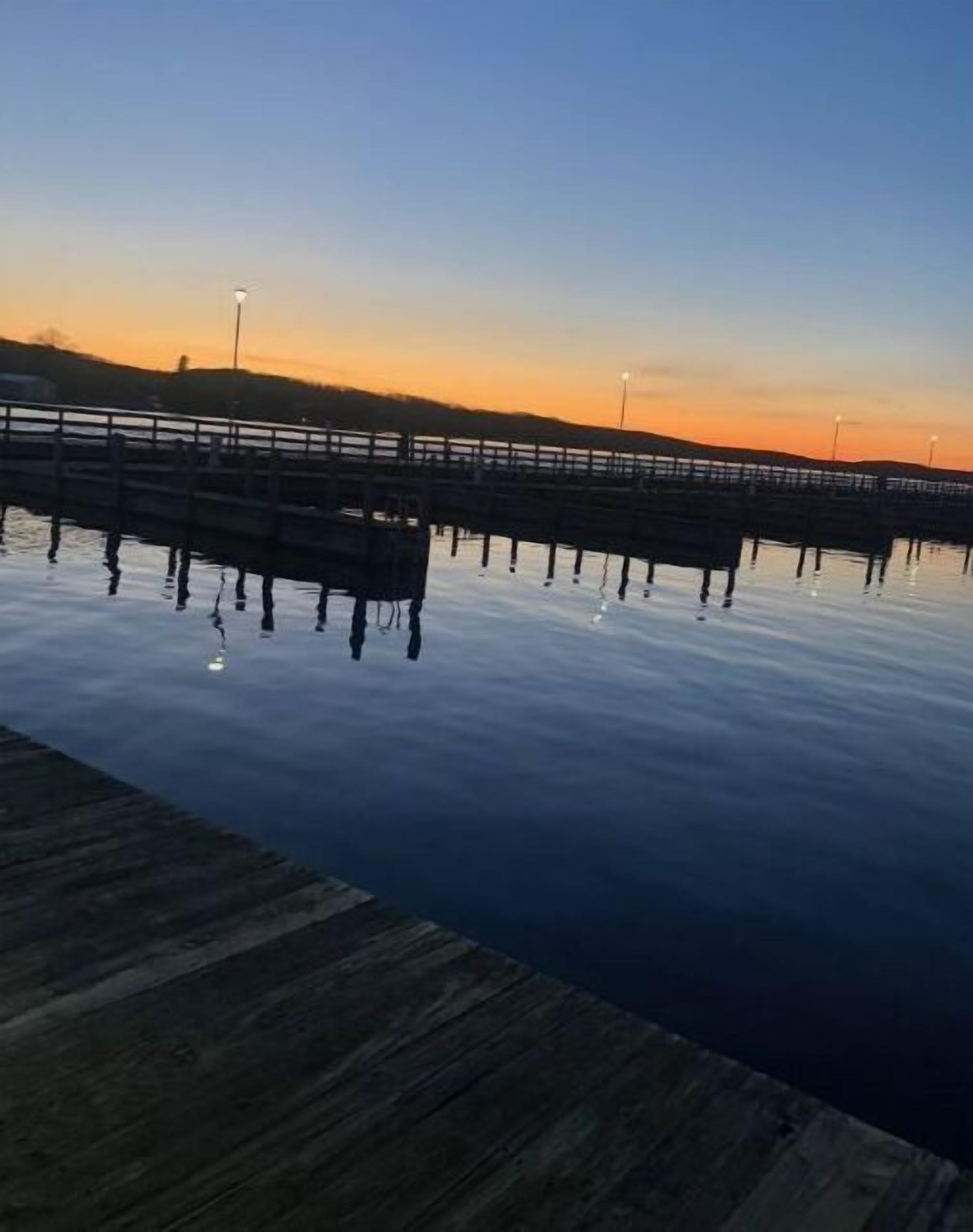 Eine Holzstege, der sich in ruhiges Wasser erstreckt, mit einem Sonnenuntergang im Hintergrund.