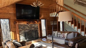 A cozy log cabin interior with a stone fireplace, leather sofas, and a staircase. - Spacious kid-friendly chalet minutes to Boone, Blowing Rock, Blue Ridge Pkwy (Boone)