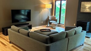 A modern living room with a sectional sofa, a flat-screen TV, a floor lamp, and a fireplace. - Spacious kid-friendly chalet minutes to Boone, Blowing Rock, Blue Ridge Pkwy (Boone)