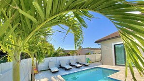En swimmingpool med vita solstolar, ett vitt staket och en palm.