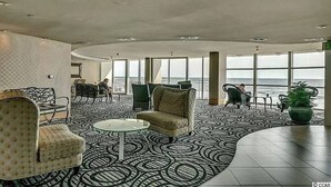 Un vaste espace de détente doté d’un sol à motifs, de différents coins salon et de grandes fenêtres offrant une vue sur la mer.