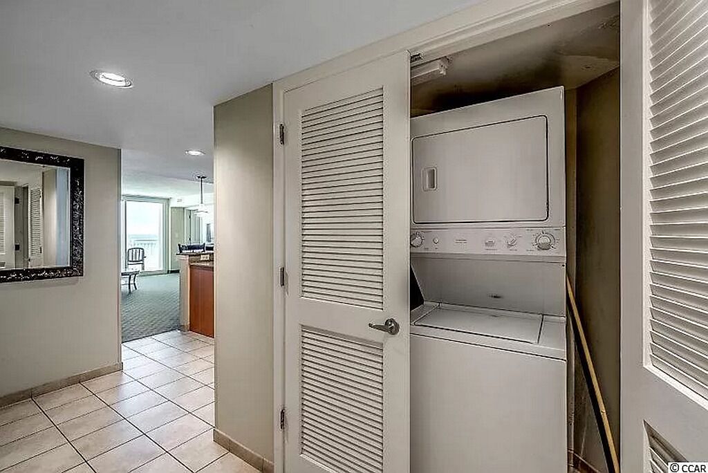 Un cuarto de lavandería con lavadora y secadora, un espejo y una puerta que da a otra habitación.