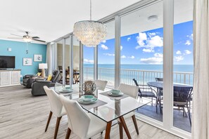 A spacious living area with a large glass table, white chairs, and a view of the ocean. - 2 KING SUITES, PENTHOUSE LEVEL, 28' WALL OF WINDOWS, BEACH VIEW & 5-STAR REVIEWS (Gulf Shores)