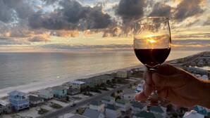 Una mano sosteniendo una copa de vino con vista al atardecer sobre un pueblo costero.