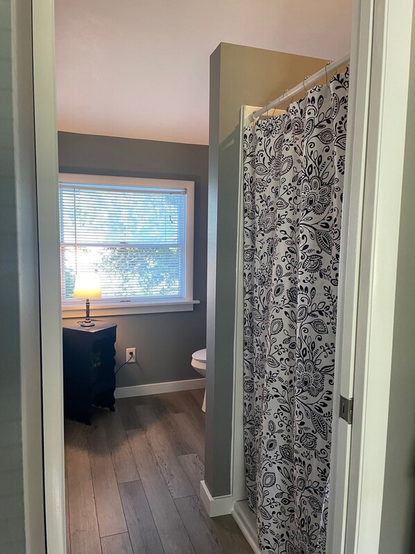 A bathroom with a window, a toilet, a vanity with a lamp, and a shower curtain with a paisley pattern. - Lilly on Lake Charlevoix (East Jordan)