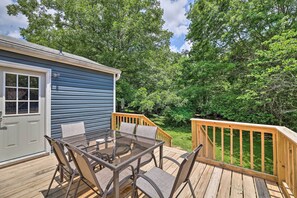 A deck with a glass table and chairs, surrounded by wooden railings and lush greenery. - Updated Fayetteville Home < 2 Miles to UArk! (Fayetteville)
