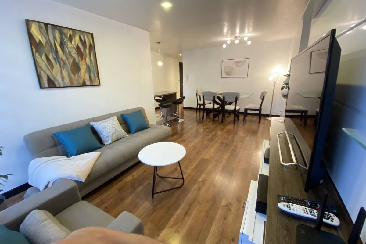 Uma sala de estar moderna com um sofá cinzento, uma mesa de centro redonda e uma TV sobre um suporte de madeira.