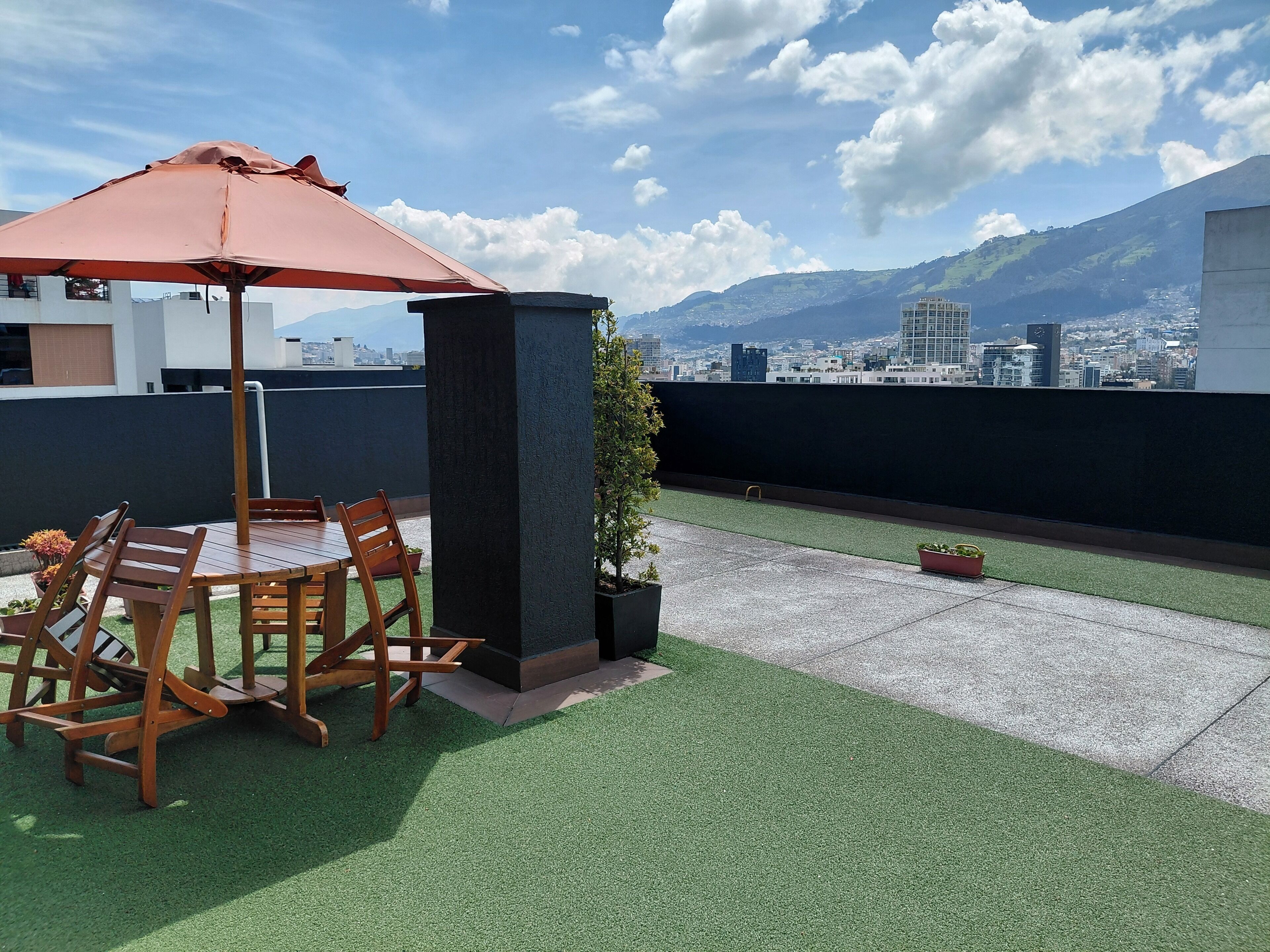 A rooftop terrace with a table and chairs, a potted plant, and a view of a cityscape and mountains.