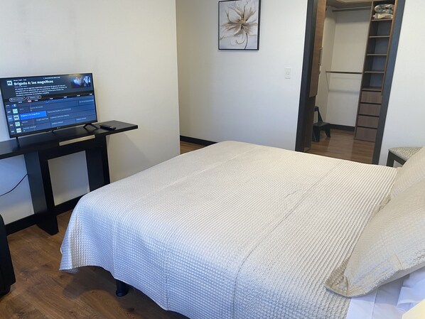 A bedroom with a bed, a desk with a computer, a wall art piece, and a closet.