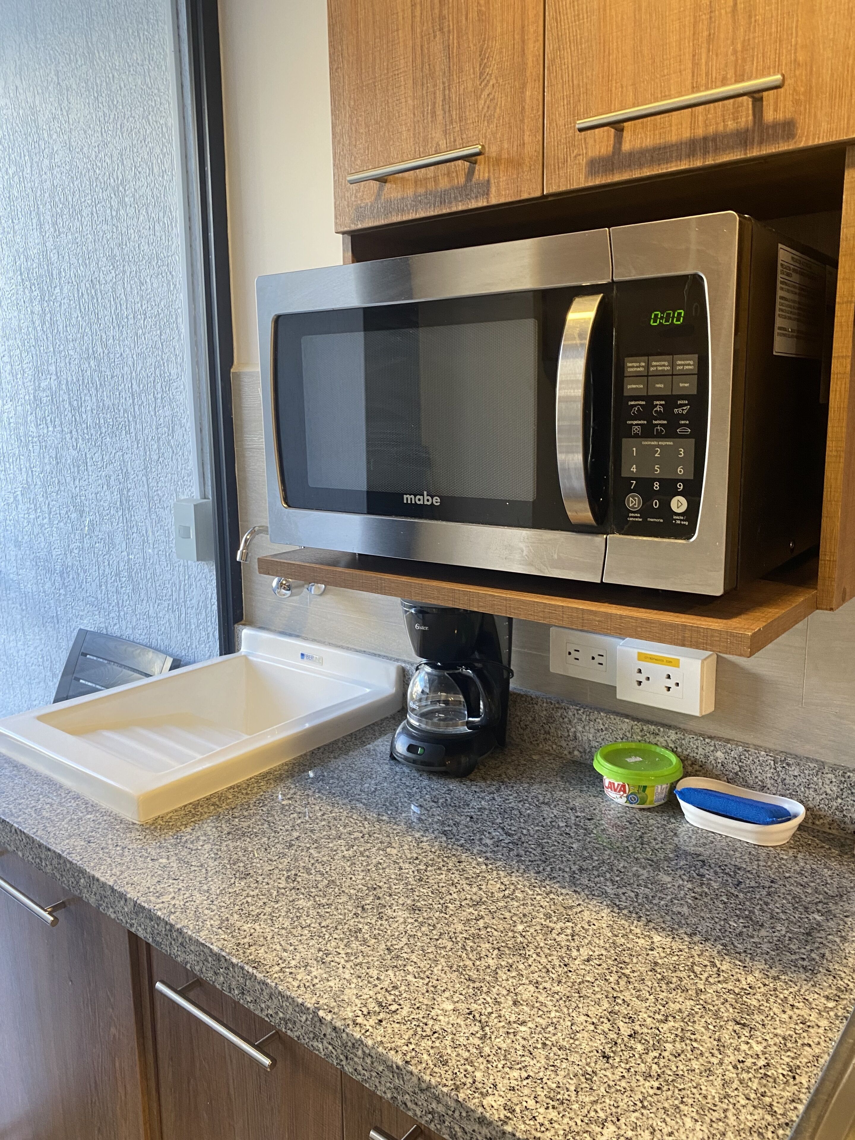 A kitchen with a built-in microwave, a coffee maker, and a small sink.
