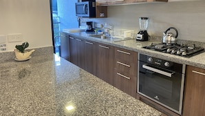 Una cocina moderna con encimeras de granito, armarios de madera, microondas integrado, cafetera, hervidor y estufa.