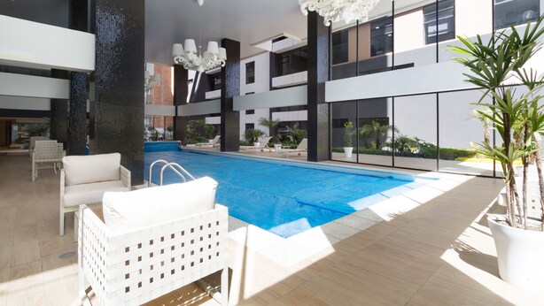 Una piscina interior moderna con sillones blancos para tomar el sol y una gran lámpara de araña.