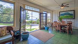 A spacious room with a large open door leading outside, a dining area with wooden furniture, and a ceiling fan. - 500 Feet to the Ocean!  (Koloa)