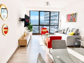 Ein modernes Wohnzimmer mit einem großen Fenster, einem Flachbildfernseher und Blick auf die Stadt.