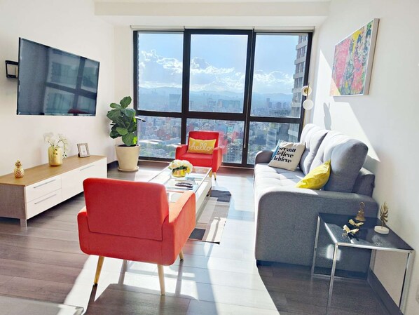 A modern living room with a sofa, armchairs, a coffee table, and a TV mounted on the wall.